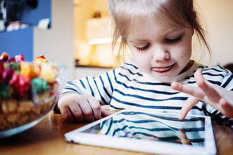 Enthusiastic little girl playing kid's study game using wireless tablet computer. Toddler growing with gadget in cozy place