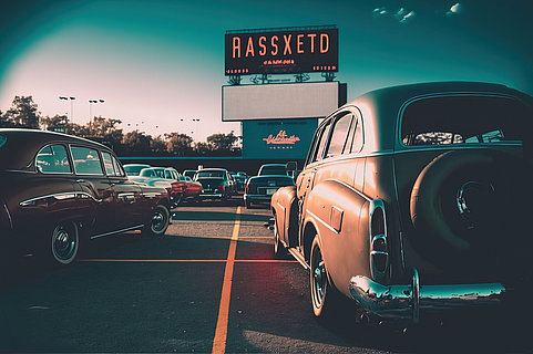 Outdoor drive-in cinema with cars in parking lot.