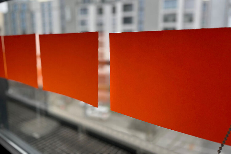 Drei orangefarbene Haftnotizen sind an einem Fenster befestigt, wobei im Hintergrund eine unscharfe Stadtlandschaft und Gebäude zu sehen sind.