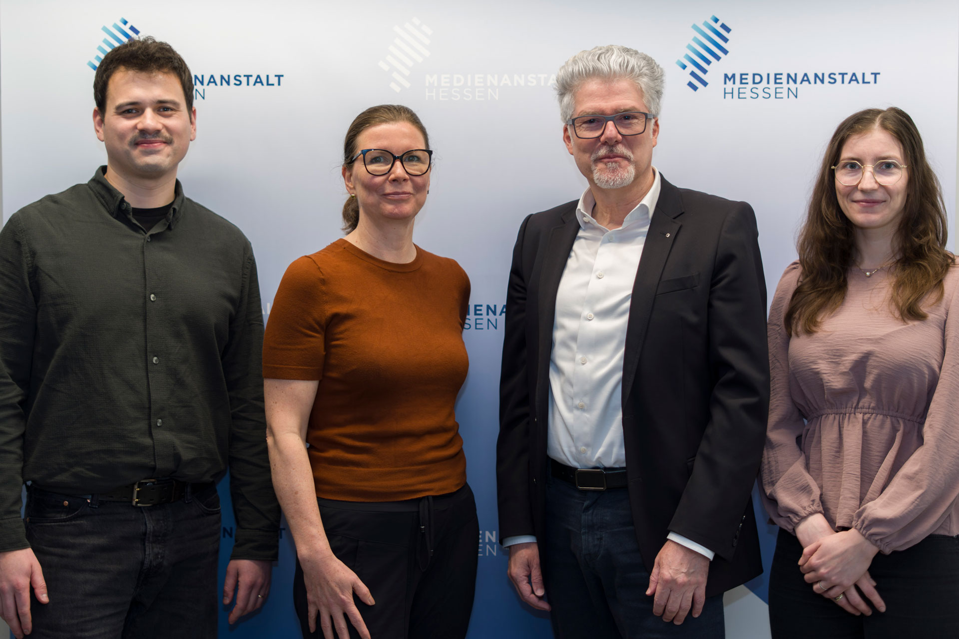 Vier Personen stehen nebeneinander vor einer hellen Wand mit dem Logo „Medienanstalt Hessen“. Von links nach rechts: Tim Ellrich, Katrin Raap, Prof. Dr. Murad Erdemir und Kerstin Waldeck. Es handelt sich um ein Gruppenfoto in einem offiziellen, beruflichen Kontext. © Medienanstalt Hessen